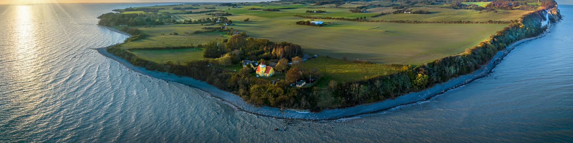 View of Møn lighthouse, distinguished by its striking yellow tower, white gallery, and vibrant red-roofed lantern and pebble beach at Møn’s south-eastern point where the majestic Møns Klint rises.