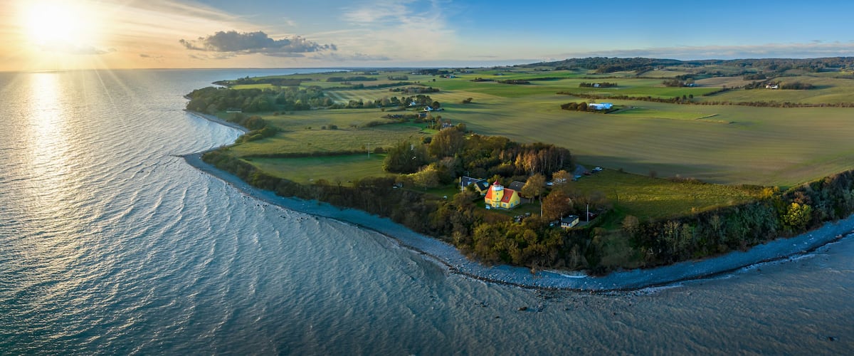 An aerial view of a coastal landscape with a prominent lighthouse, rolling hills, and a clear sky.