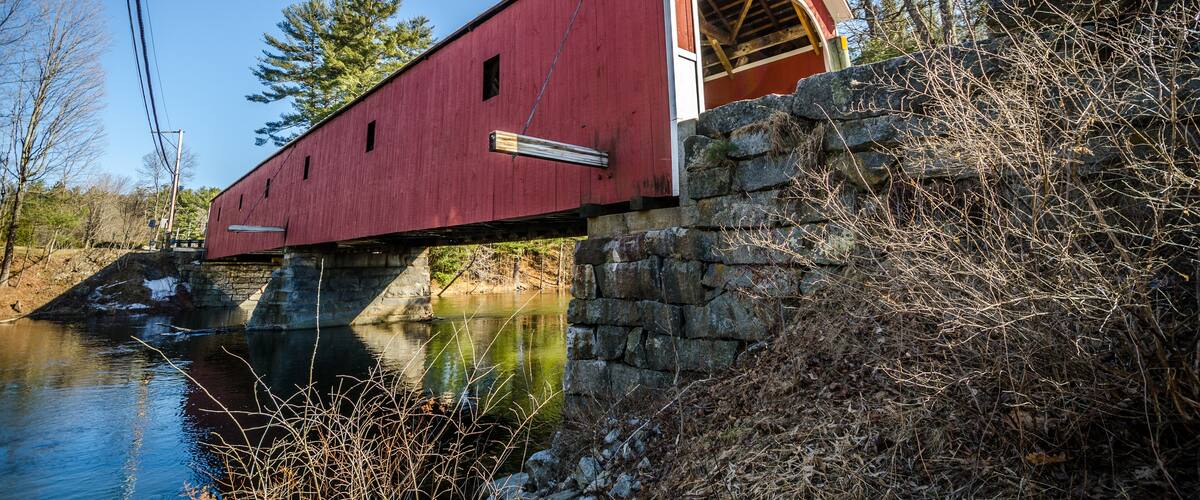 A red covered bridge over a river, surrounded by trees and stone walls.