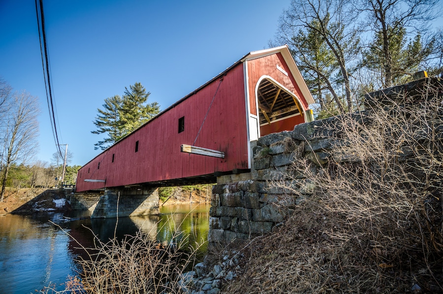 A red covered bridge over a river, surrounded by trees and stone walls.