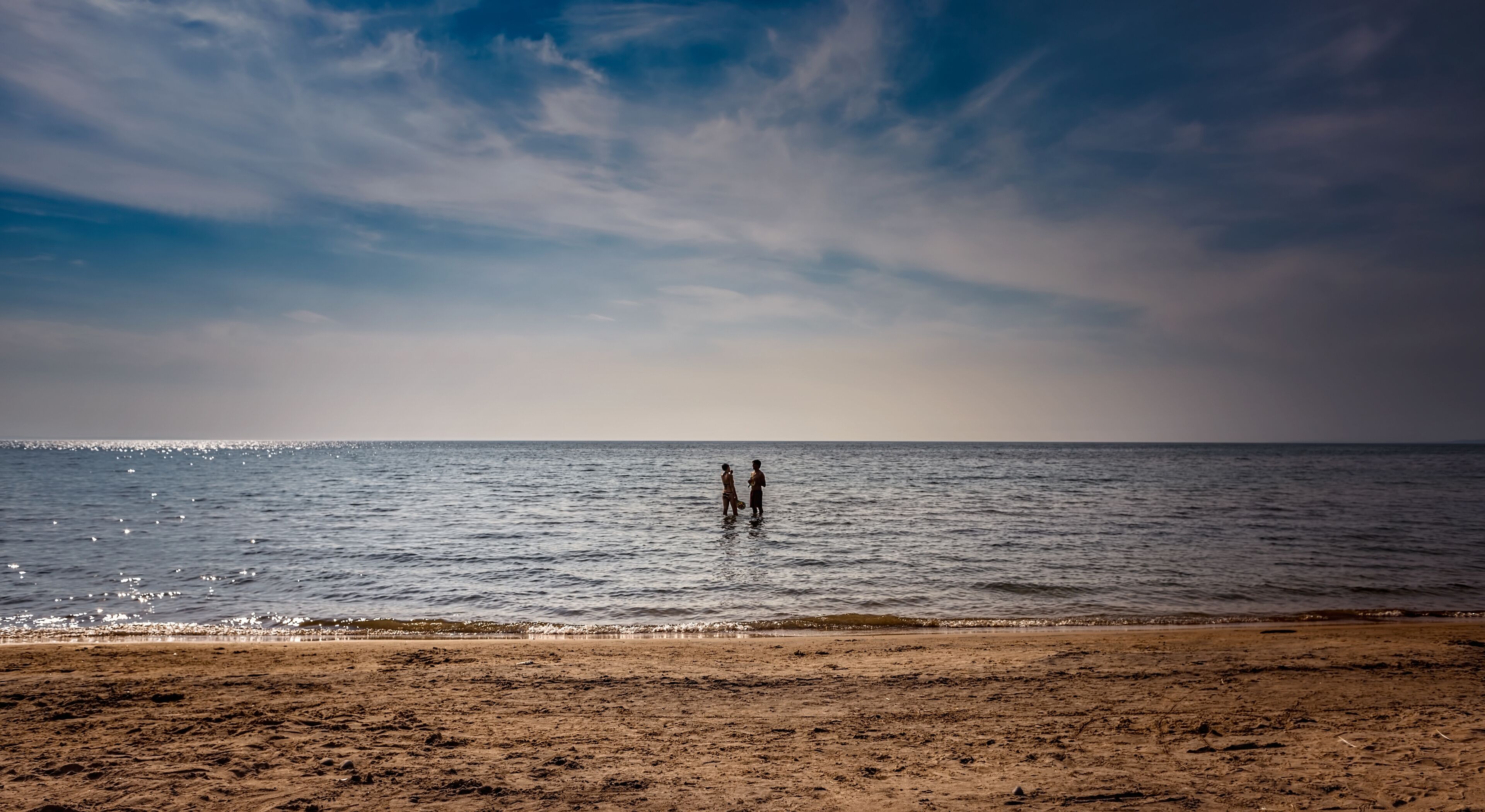 A beach with two people standing in shallow water.
