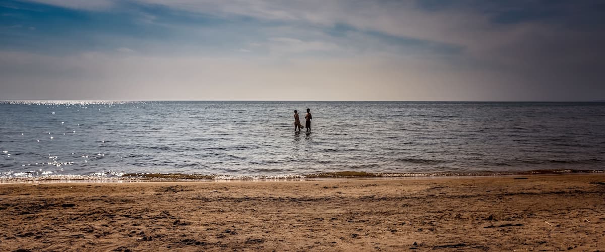 A beach with two people standing in shallow water.