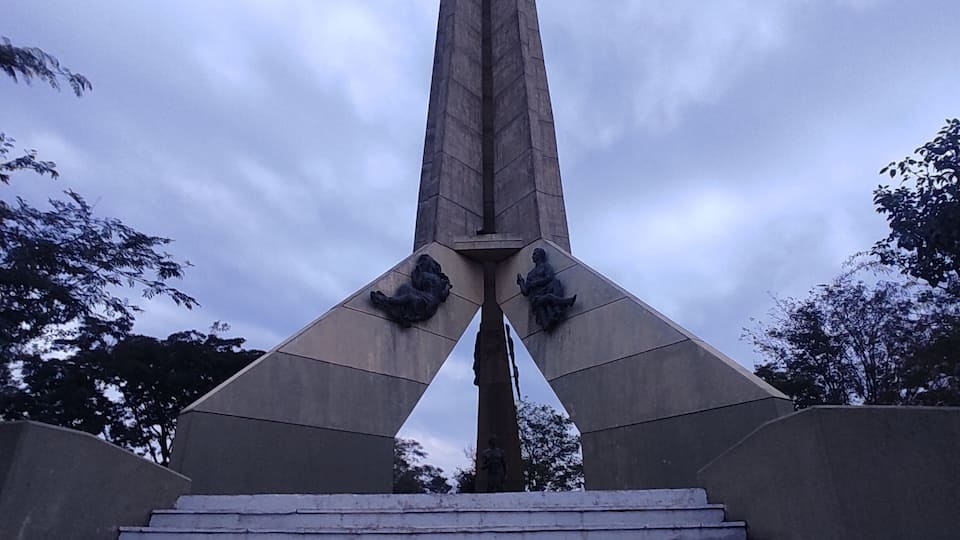 A monument with a tall central pillar and wings on either side, with steps leading up to it.