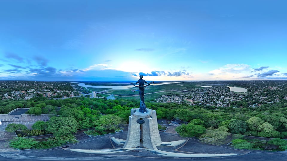 A statue on a pedestal overlooking a city with a river and greenery.