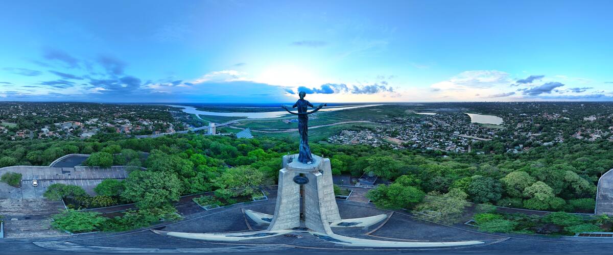 A statue on a pedestal overlooking a city with a river and greenery.