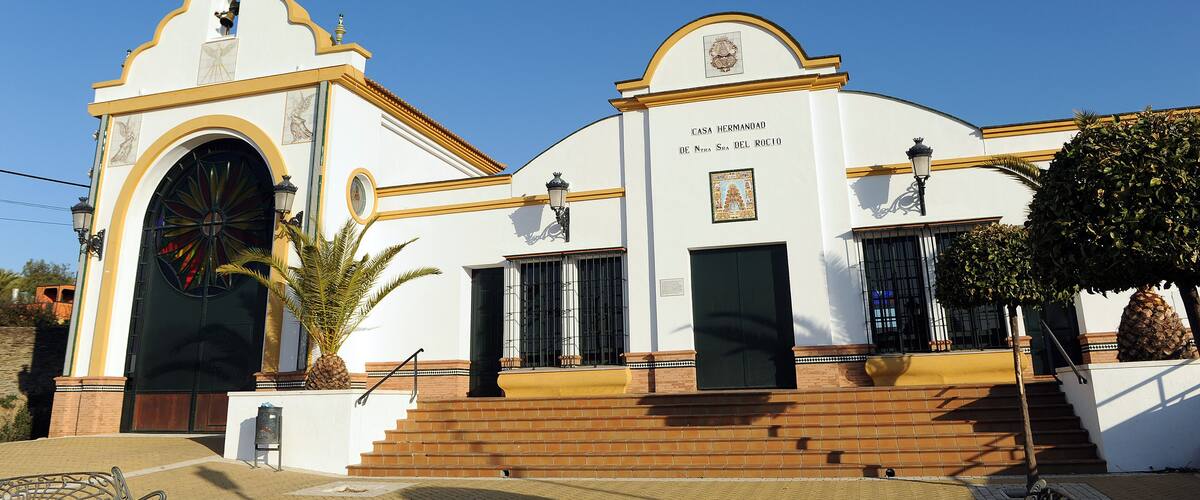 A white building with a cross on top, a large arched entrance, and a staircase leading up to the entrance.