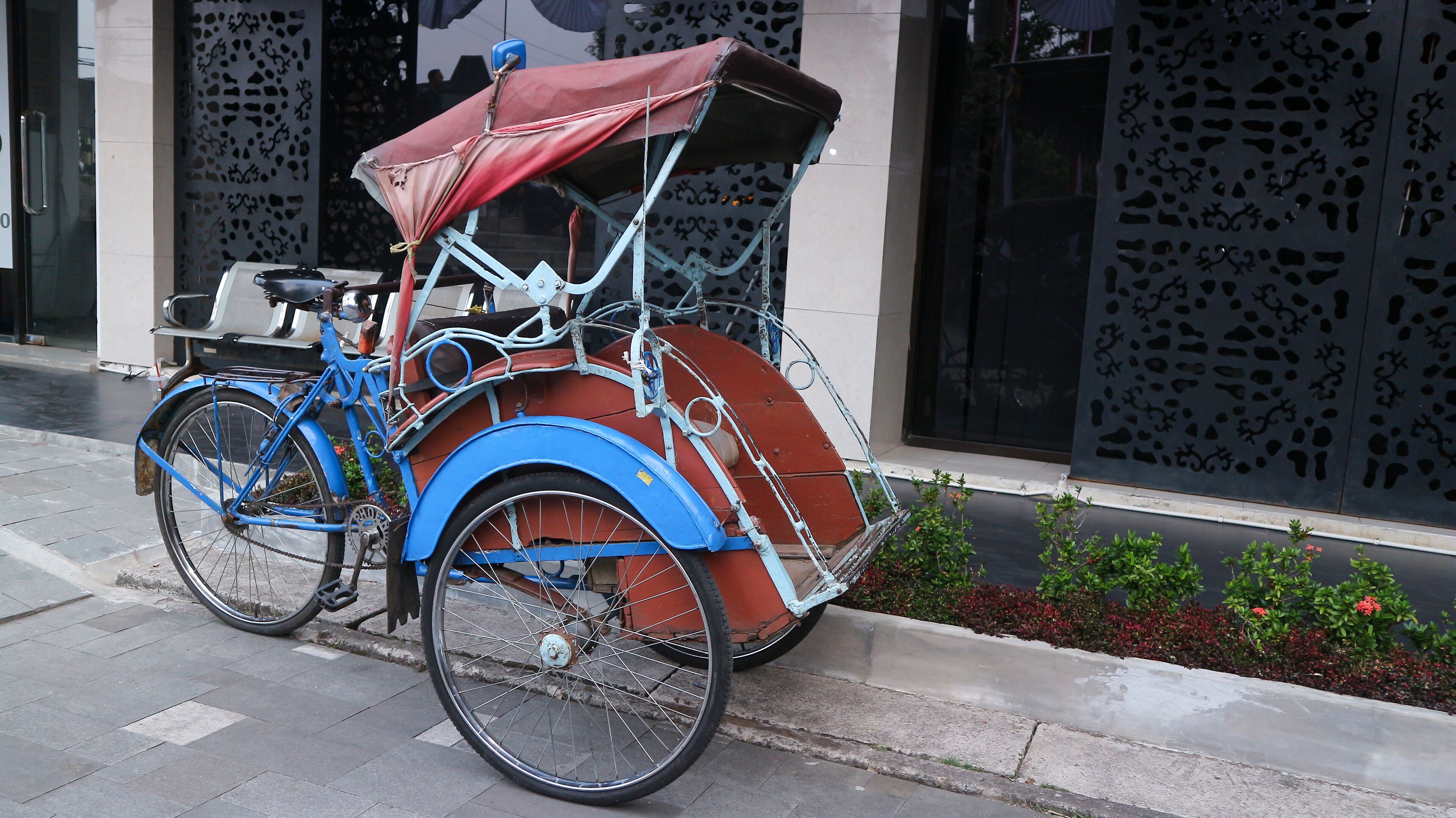 A blue and red rickshaw parked on a city sidewalk.