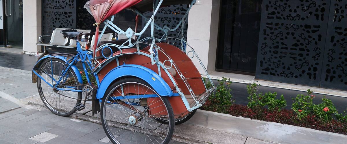 A blue and red rickshaw parked on a city sidewalk.