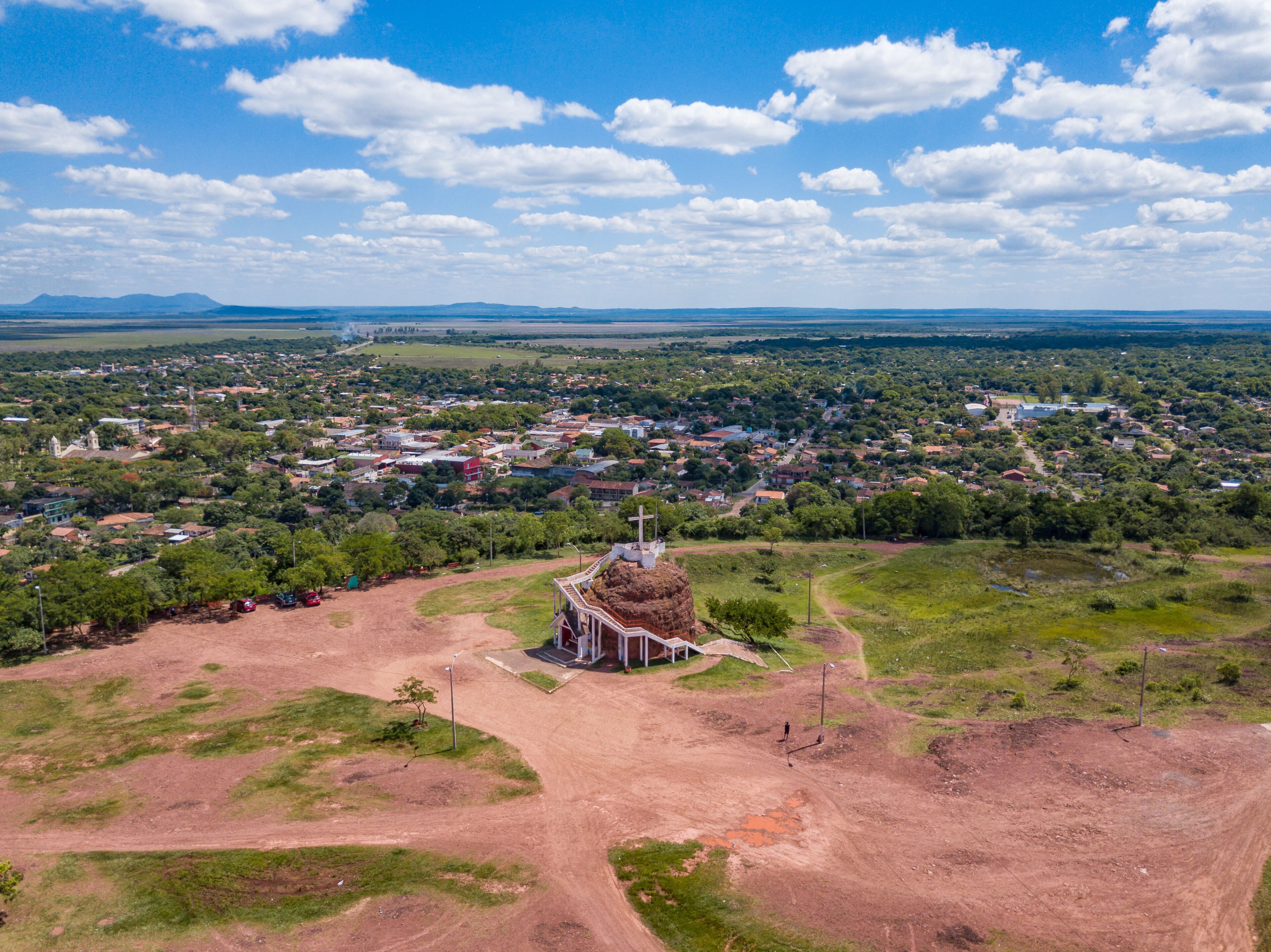 An aerial view of a town with a prominent church in the center, surrounded by greenery and a clear sky.