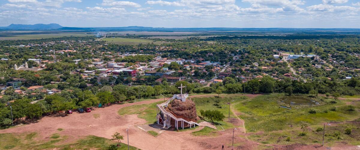 An aerial view of a town with a prominent church in the center, surrounded by greenery and a clear sky.