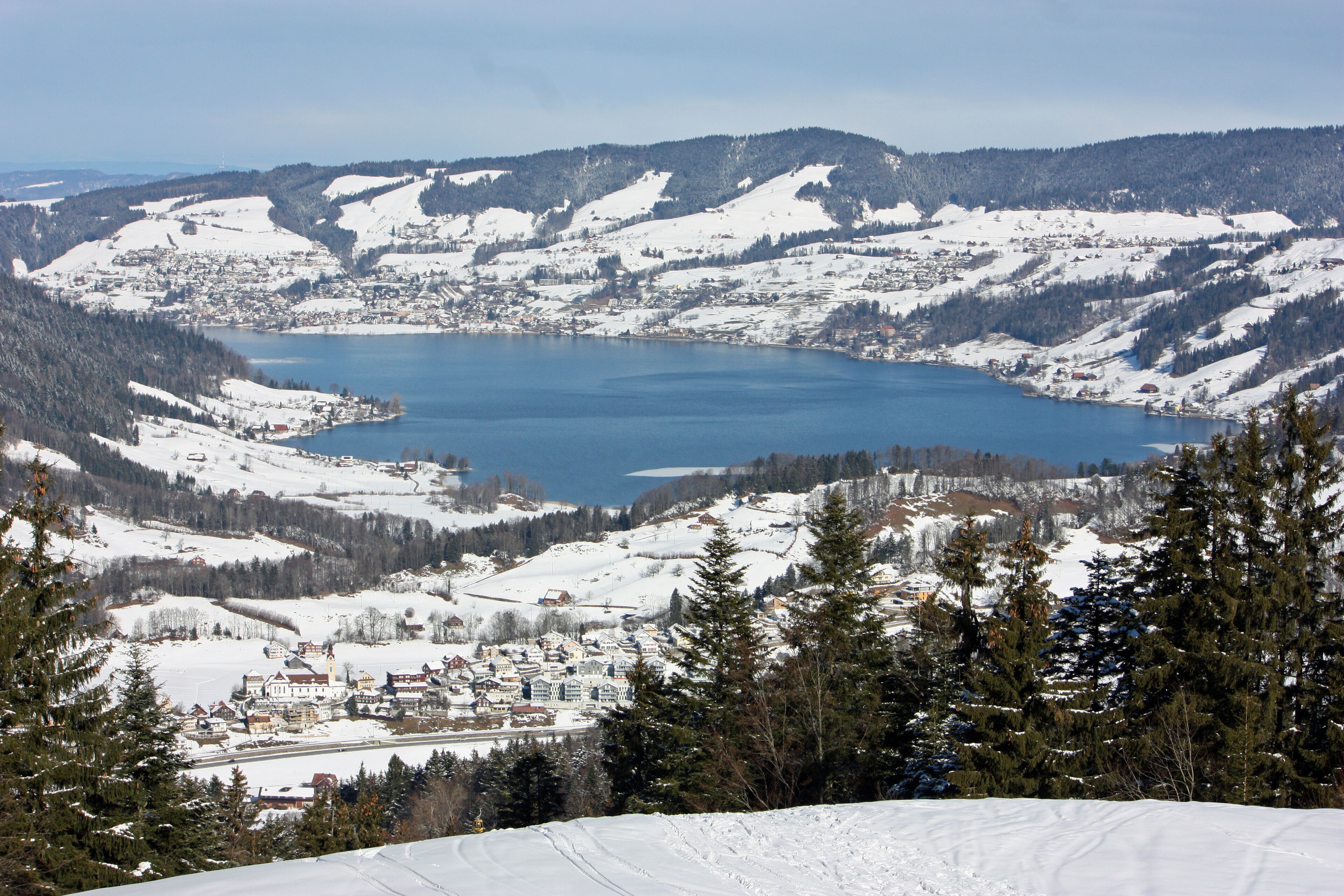 A snow-covered landscape with a lake, mountains, and a small town.