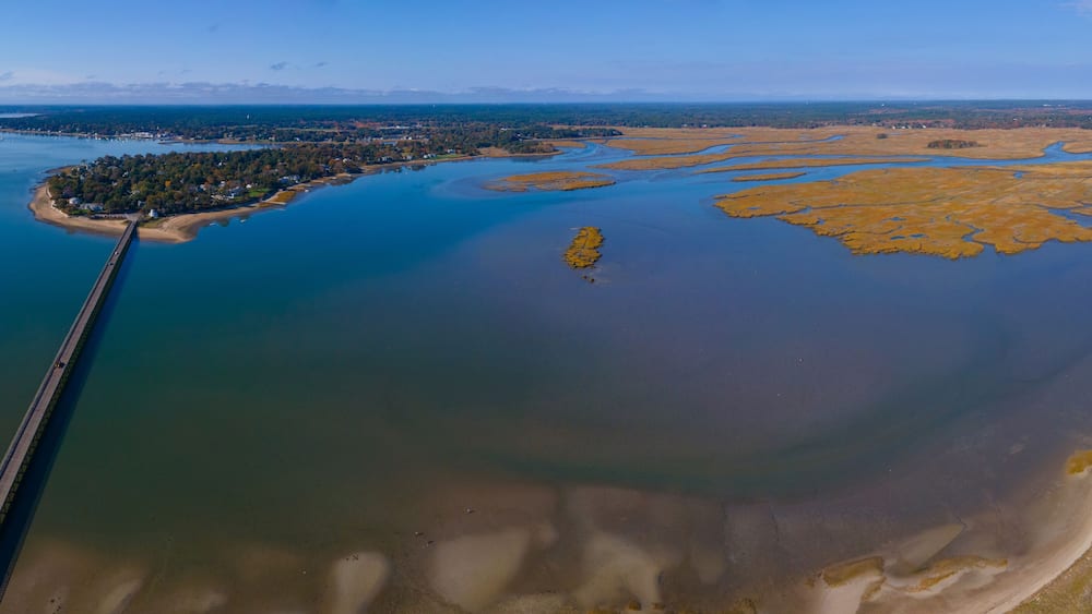 Vue aérienne d’une zone côtière avec un pont, une étendue d’eau importante et une péninsule boisée.