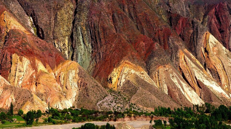 A mountain with layered rock formations and a road at the base.