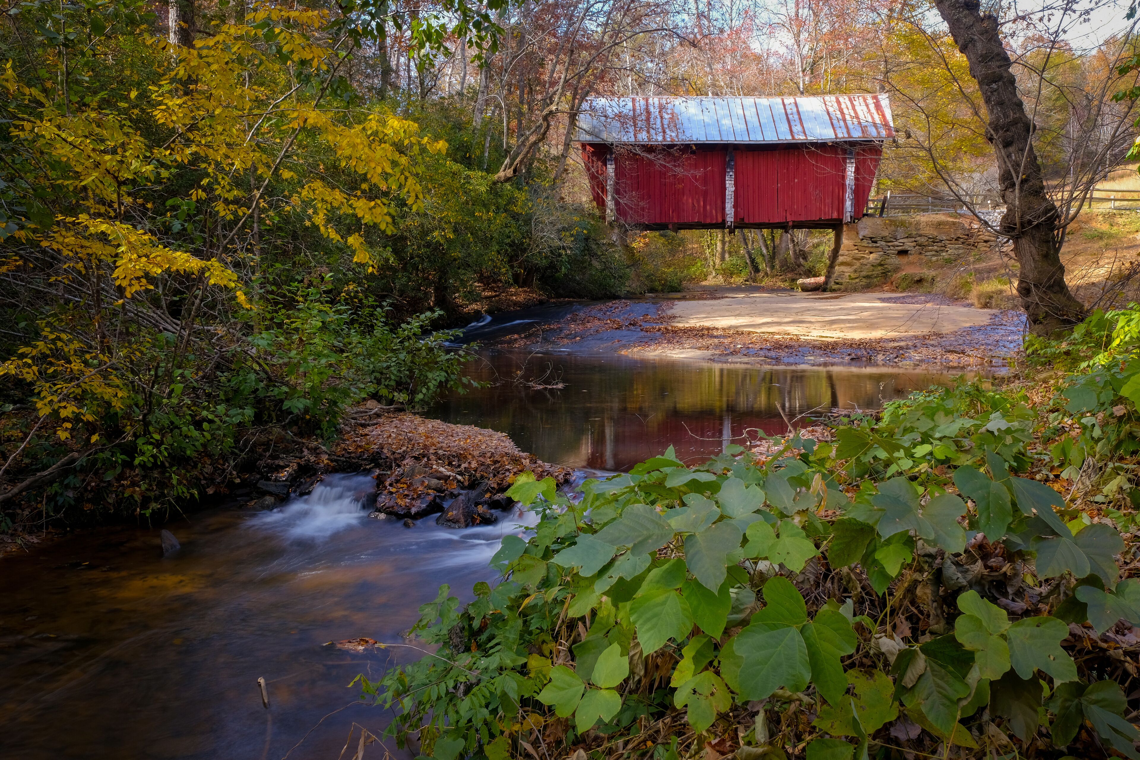 Campbell's covered bridge in Greer, South Carolina, USA with fall foliage and smooth water in stream