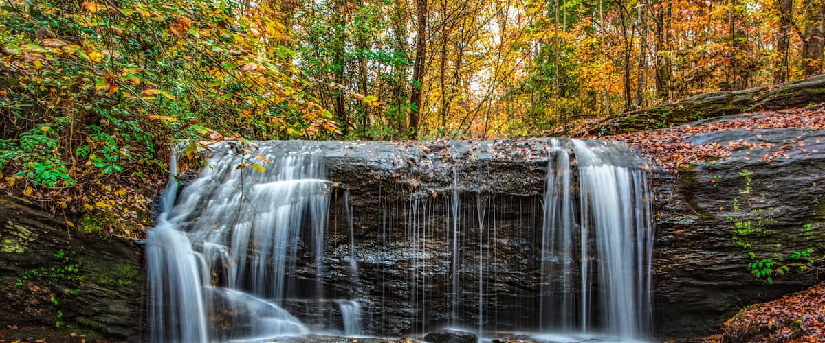 A waterfall cascading over a rocky ledge surrounded by autumn foliage.