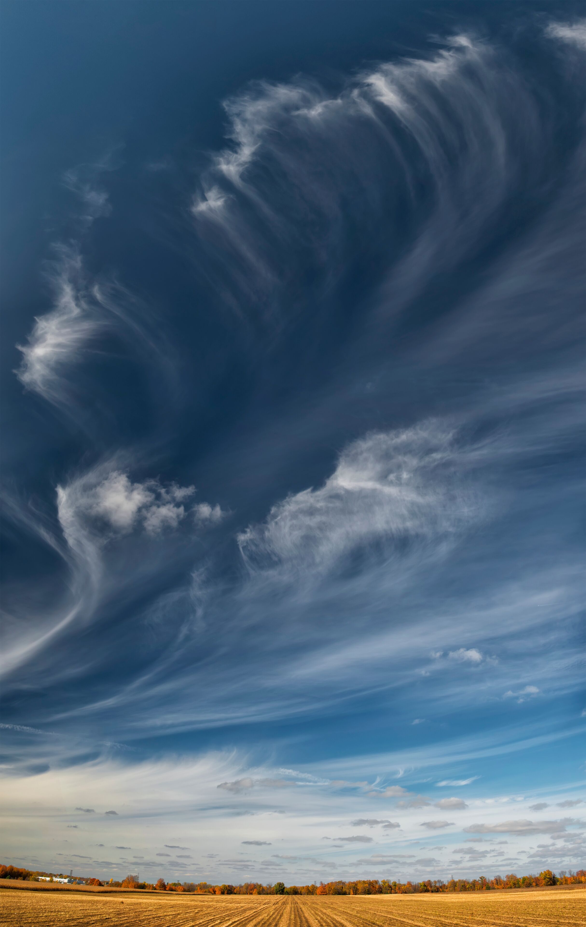 A vast field with a dramatic sky featuring a large, swirling cloud formation.
