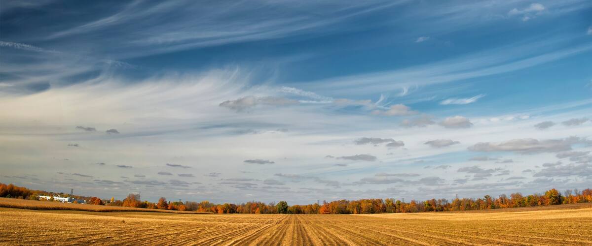 A vast field with a dramatic sky featuring a large, swirling cloud formation.