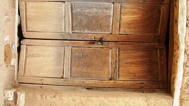 A rustic wooden door with a metal latch, set in a rough-textured wall.
