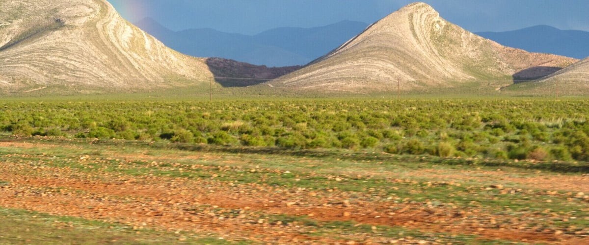 A desert landscape with rolling hills and a rainbow in the distance.