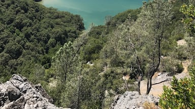 Paisagem costeira com um lago azul cristalino, rodeado por florestas densas e montanhas ao longe.