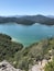 A coastal landscape with a clear blue lake surrounded by dense forests and distant mountains.