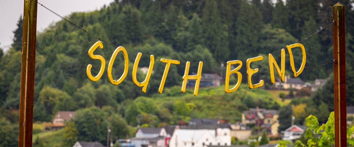 A sign reading "SOUTH BEND" with a backdrop of a town and forest.