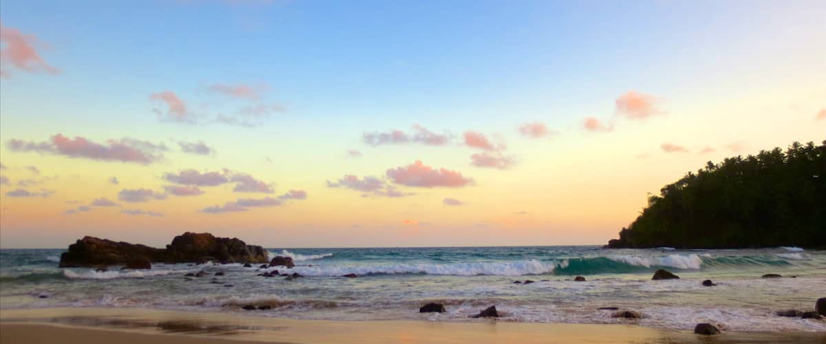 A beach with waves, rocks, and a sunset sky.