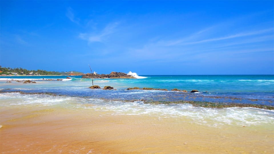A beach with clear turquoise waters, rocky outcrops, and a distant shoreline with vegetation.