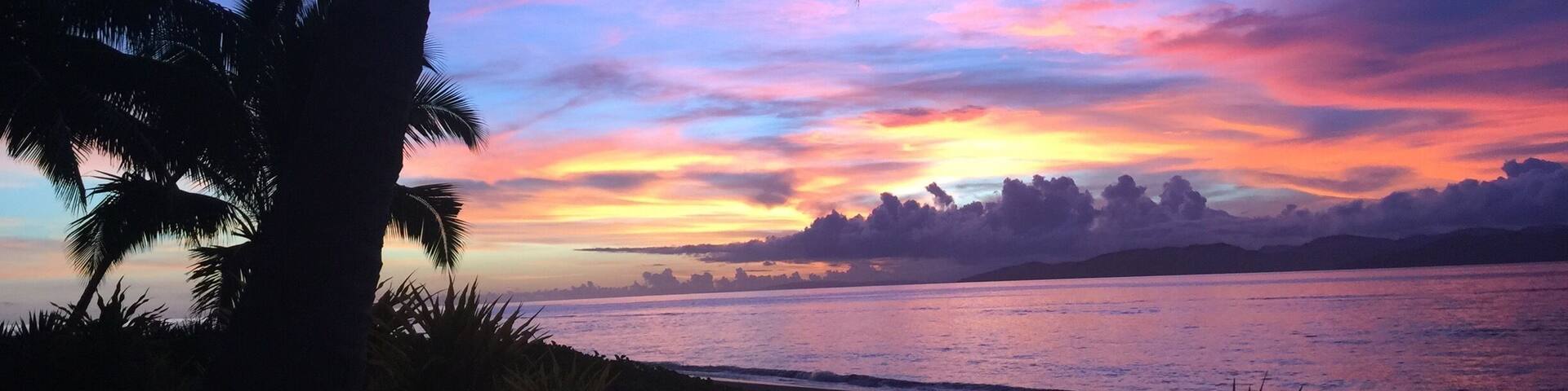 A sunset over a body of water with palm trees silhouetted against a colorful sky.