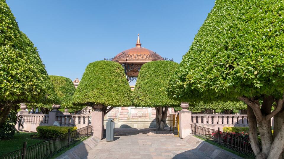 A garden with a central dome structure, surrounded by neatly trimmed hedges and trees.