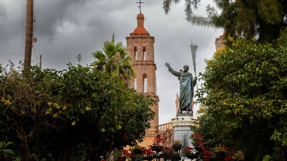 A statue in a garden with a bell tower in the background.