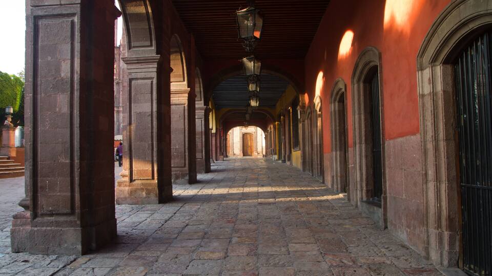 A stone-paved corridor with arches and columns, leading to a doorway.