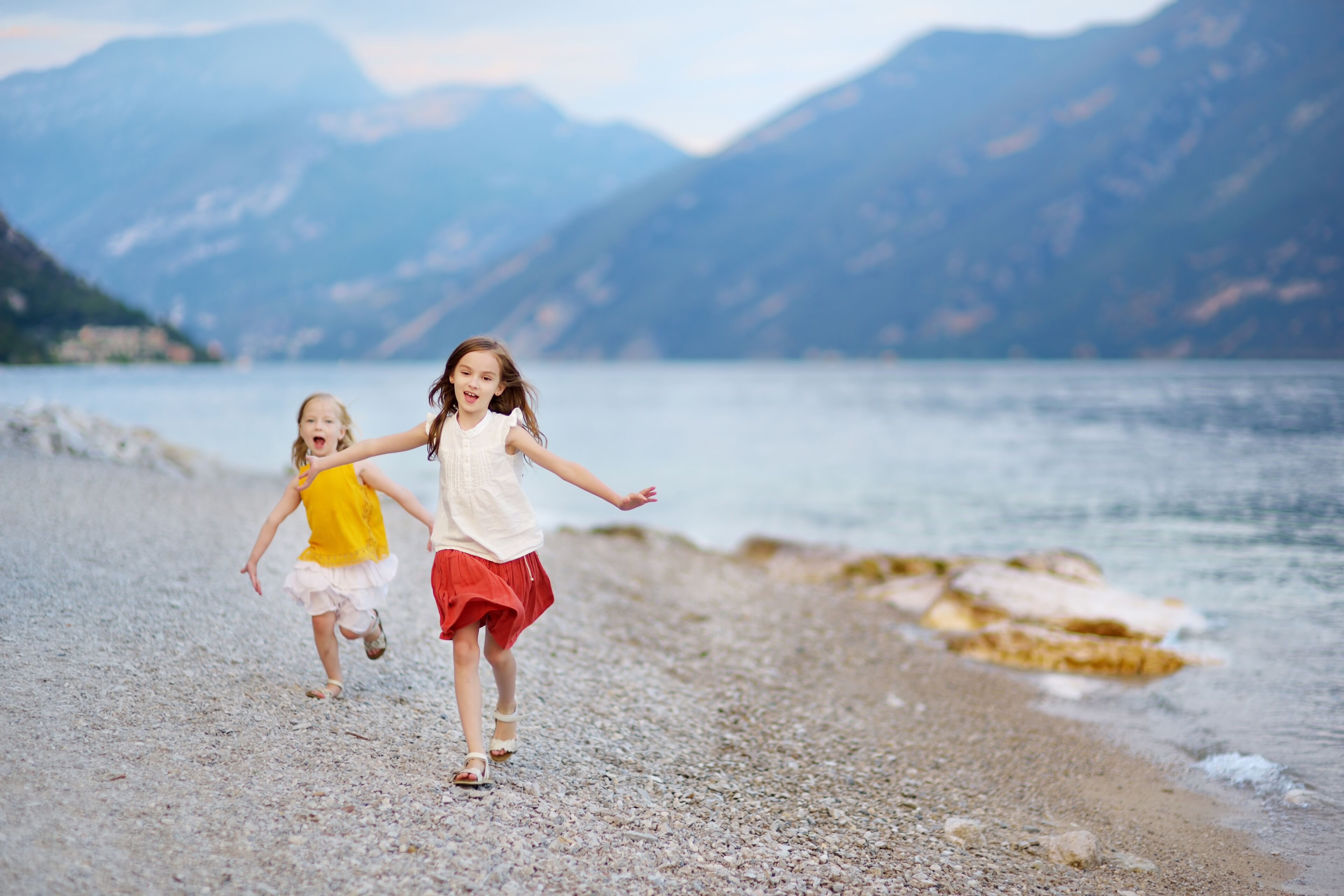 Two cute little sisters having fun on a beach of Limone sul Garda, a small town and comune in the province of Brescia, Italy