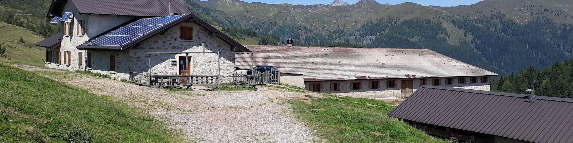 A stone building with solar panels, a gravel path, and mountainous terrain in the background.