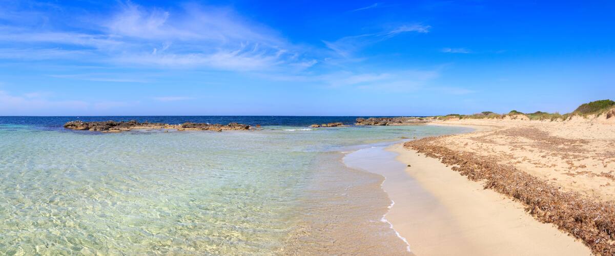 A clear beach with turquoise water, sandy shore, and rocky outcrops.