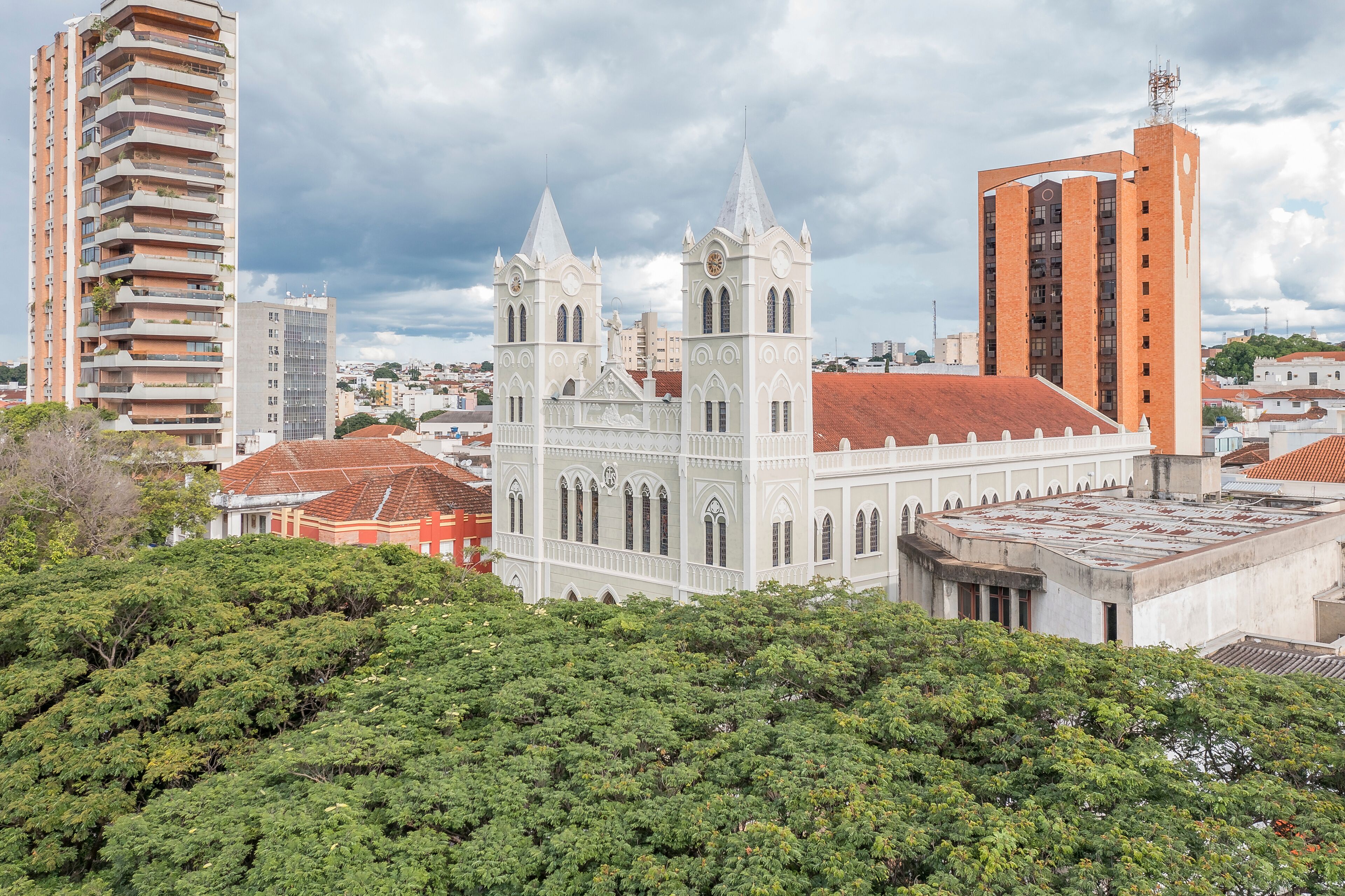 A historic church with twin spires, surrounded by modern buildings and lush greenery.