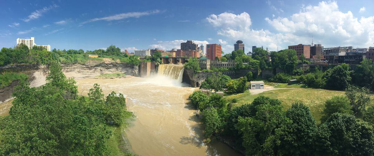 A waterfall cascading into a river surrounded by greenery and urban buildings.