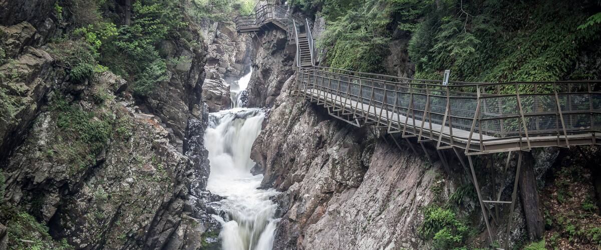 A waterfall cascading down a rocky gorge with a wooden walkway above.