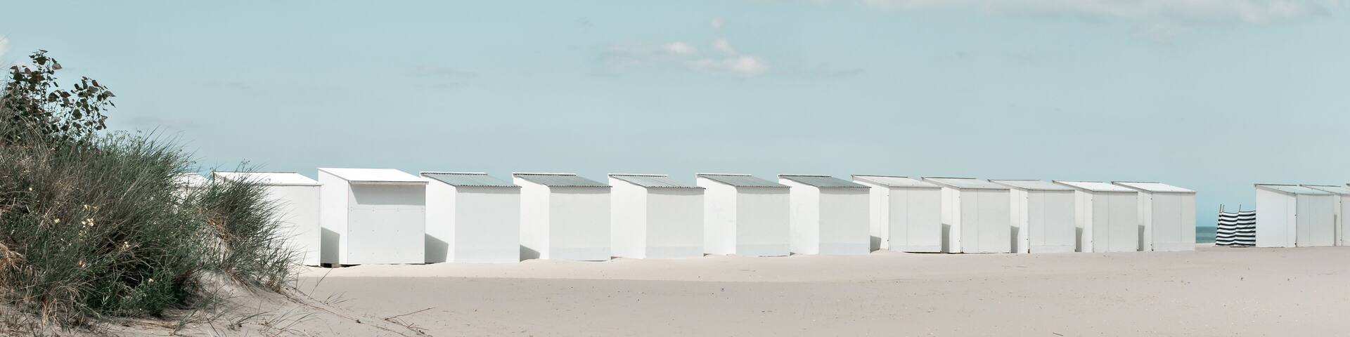 A row of white beach cabins on a summer day.