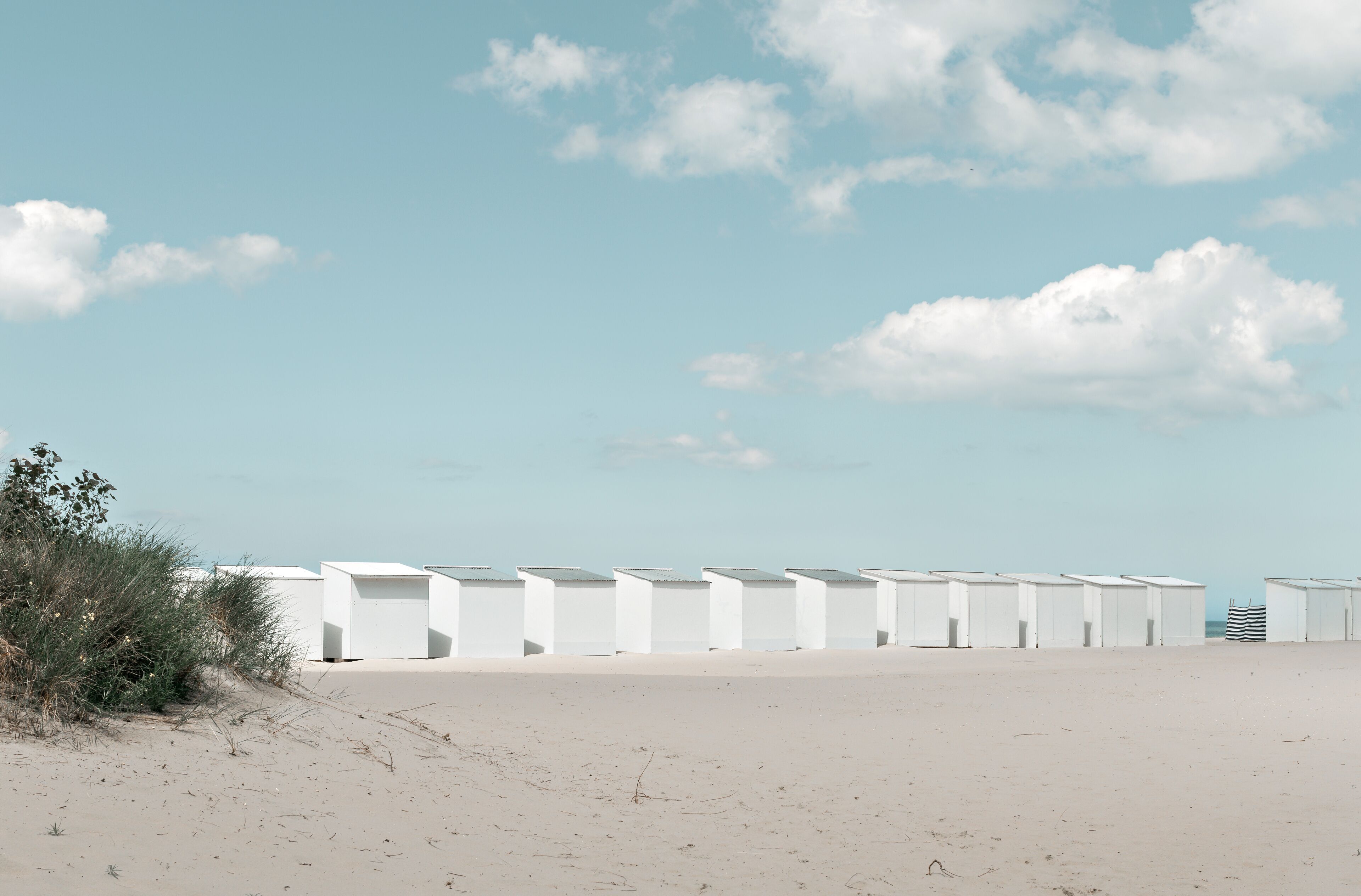 A beach with white beach huts and a clear sky.