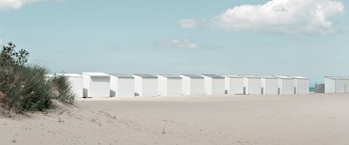 A beach with white beach huts and a clear sky.
