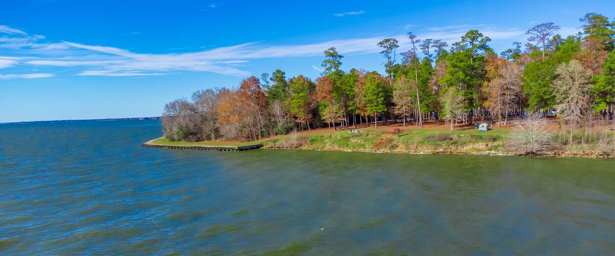 A calm lake with a forested shoreline and a clear blue sky.
