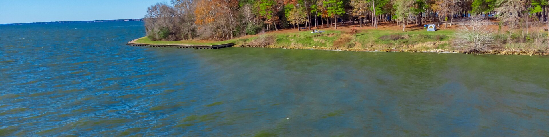 A calm lake with a forested shoreline and a clear blue sky.