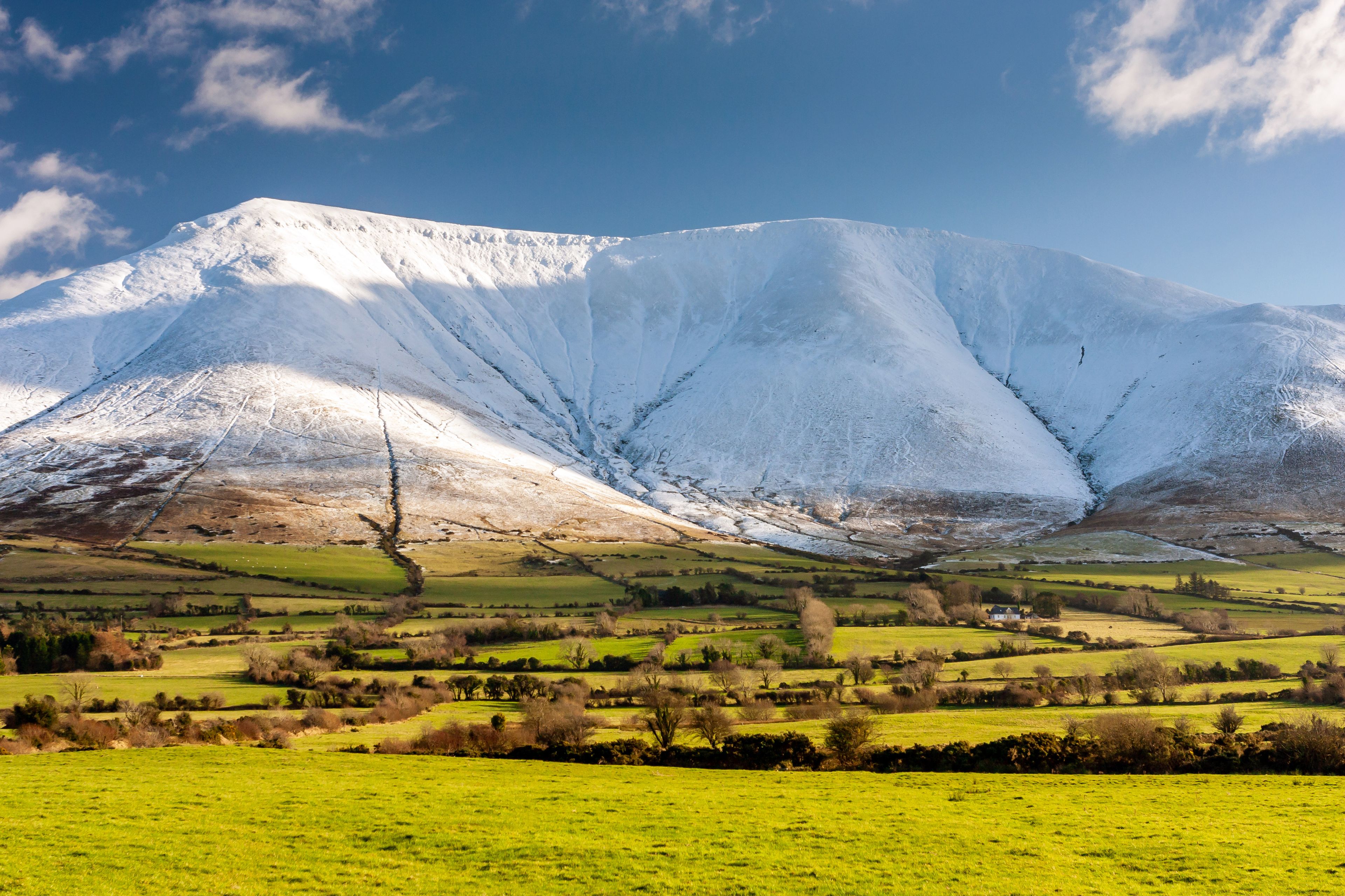 A snow-covered mountain range with a green valley in the foreground.