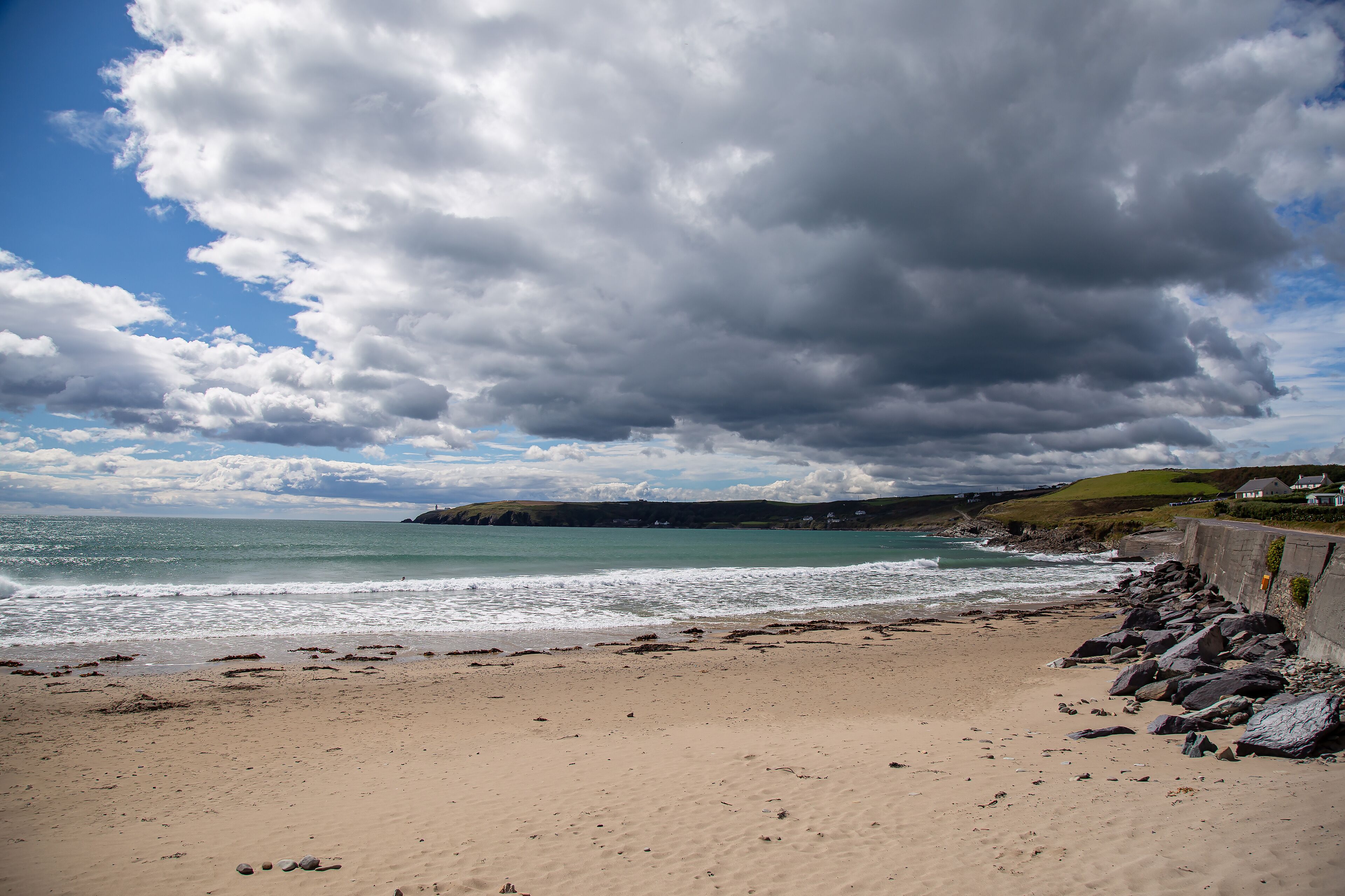 A beach with a rocky shoreline, waves crashing onto the sand, and a cloudy sky.