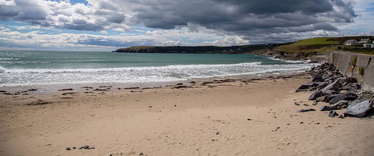 A beach with a rocky shoreline, waves crashing onto the sand, and a cloudy sky.