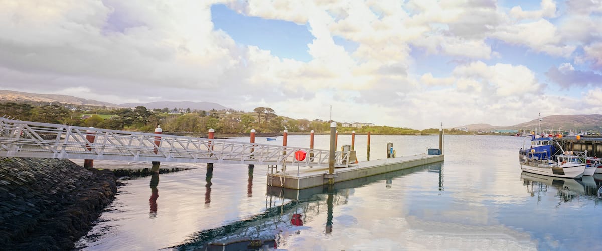 A calm harbor with a bridge, boats, and a distant mountain range under a partly cloudy sky.