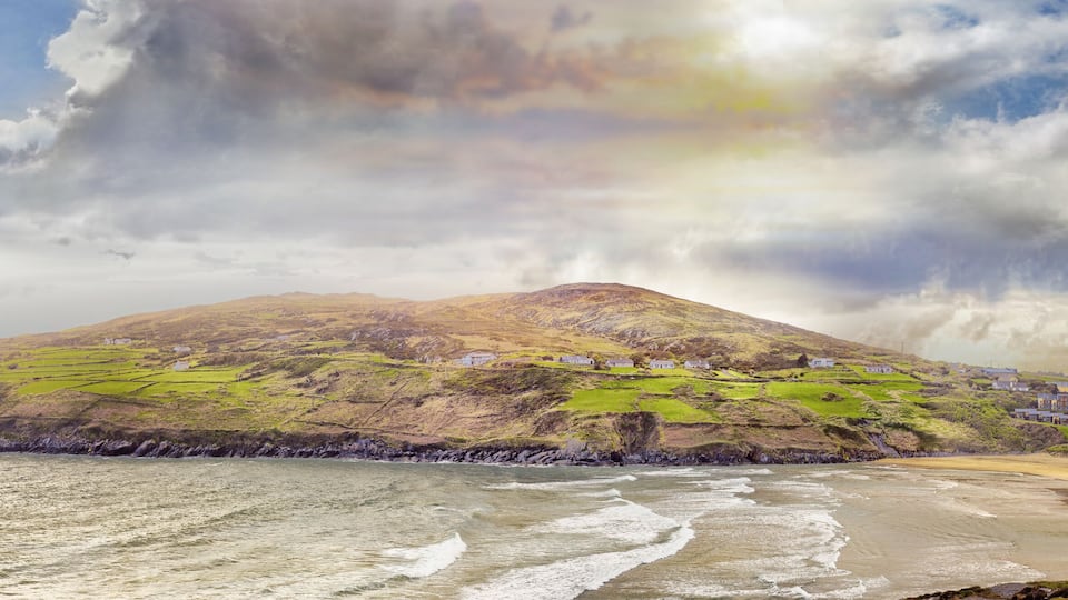 A coastal landscape with a mountain, green fields, and a beach.