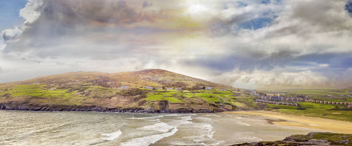 A coastal landscape with a mountain, green fields, and a beach.