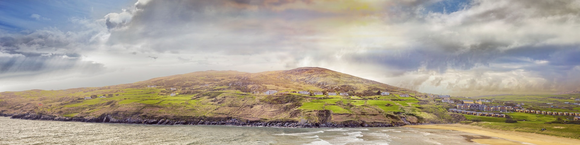 A coastal landscape with a mountain, green fields, and a beach.